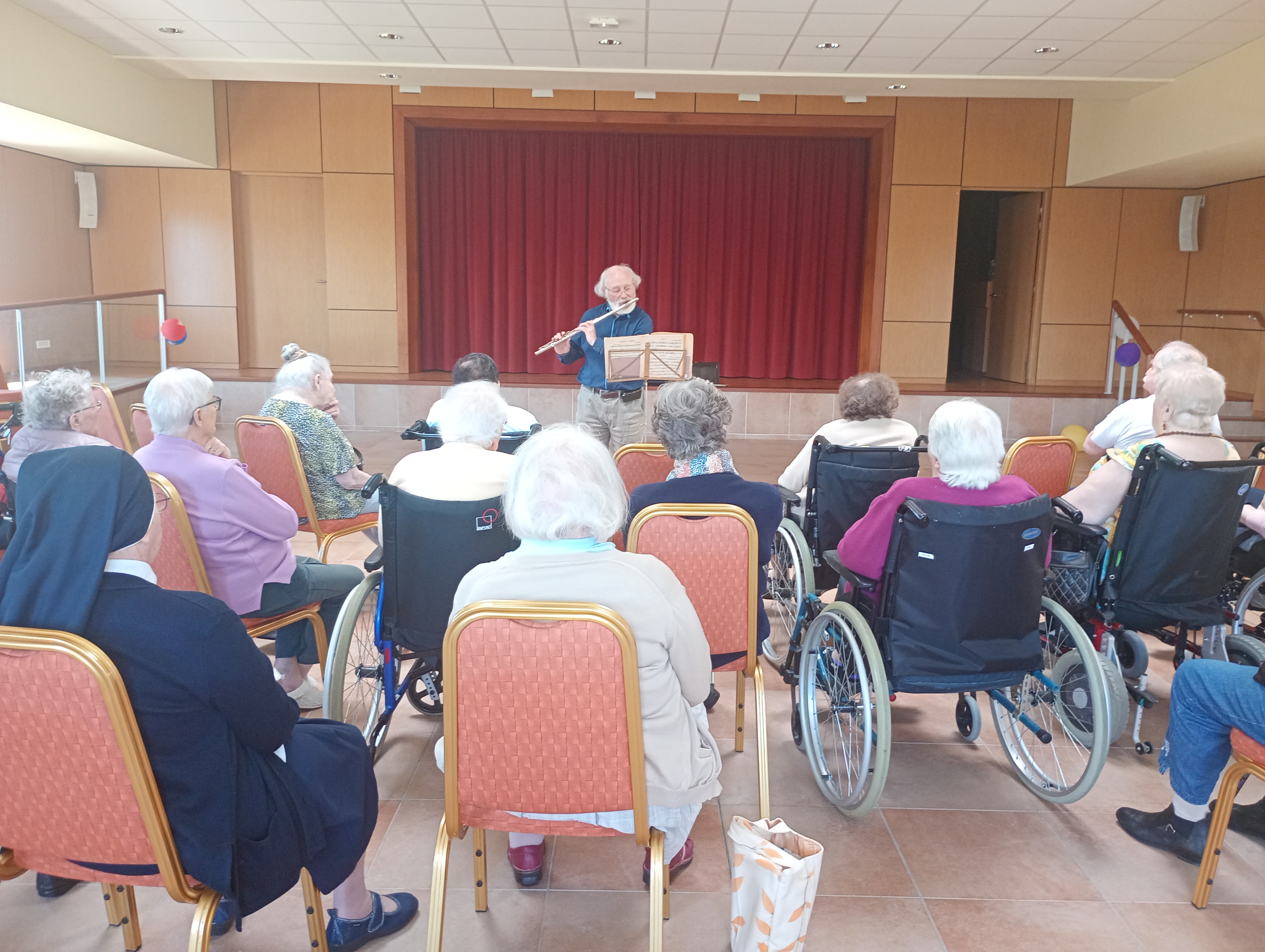 Personnes âgées dans une salle devant une personne qui joue de la flûte traversière