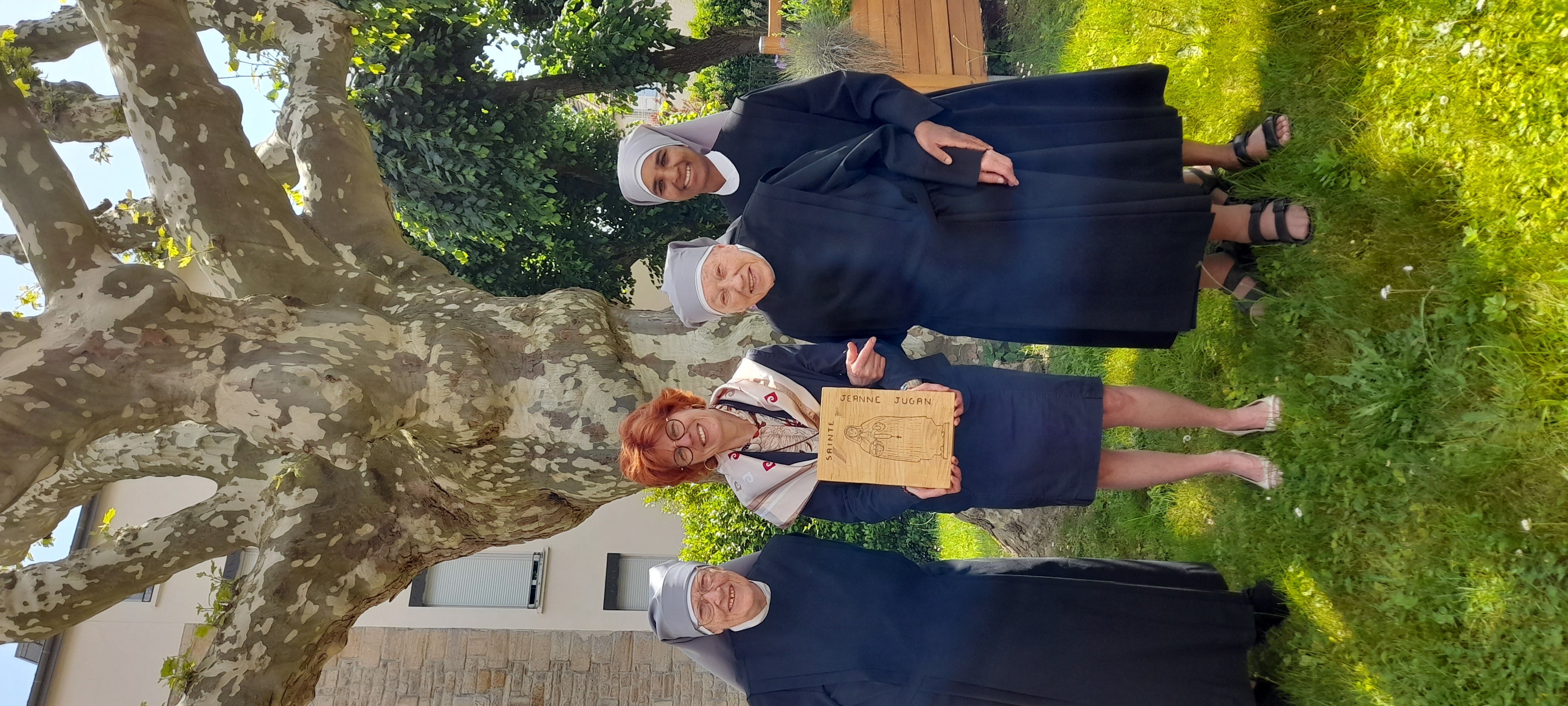 3 petites sœurs et une dame tenant un tableau de Sainte Jeanne Jugan gravée dans le bois