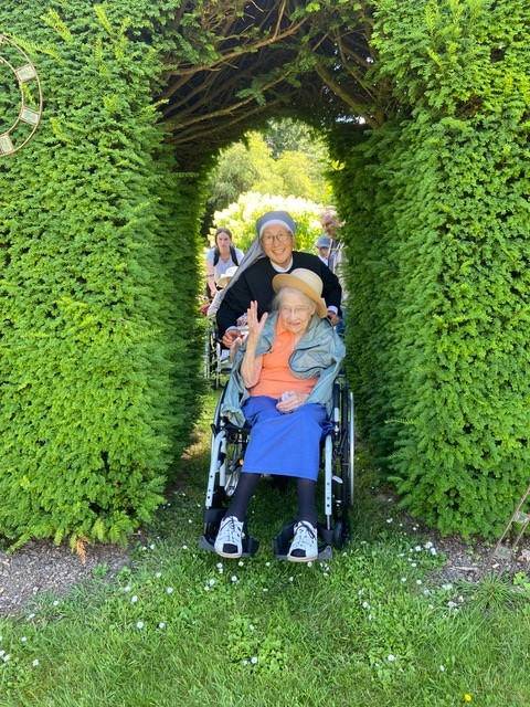 Personne âgée dans un fauteuil poussée par une bénévole dans un jardin