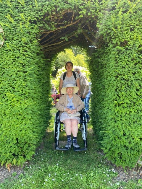 Personne âgée dans un fauteuil poussée par une bénévole dans un jardin