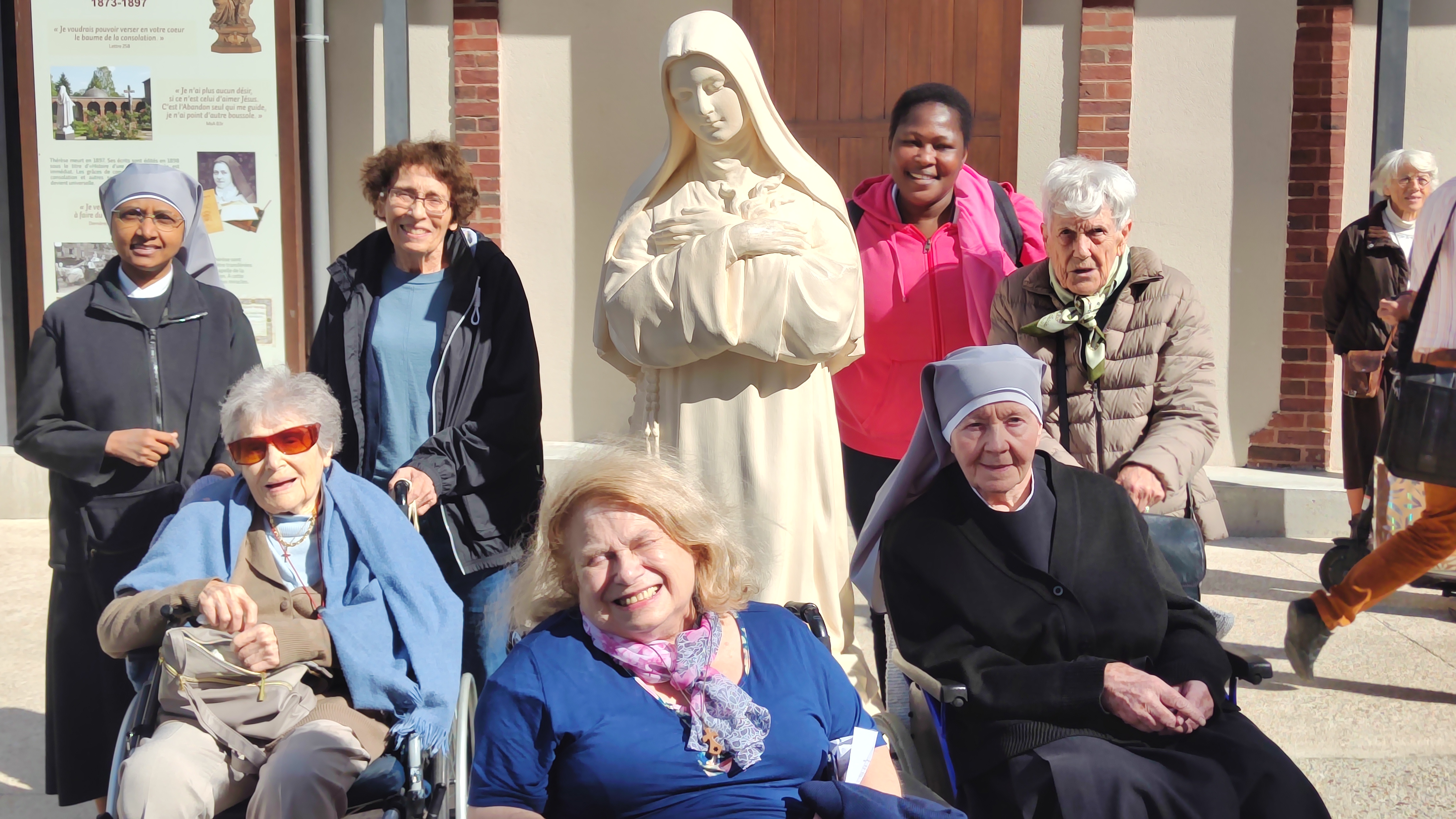Personnes âgées et petites soeurs devant un statue de sainte Thérèse de Lisieux
