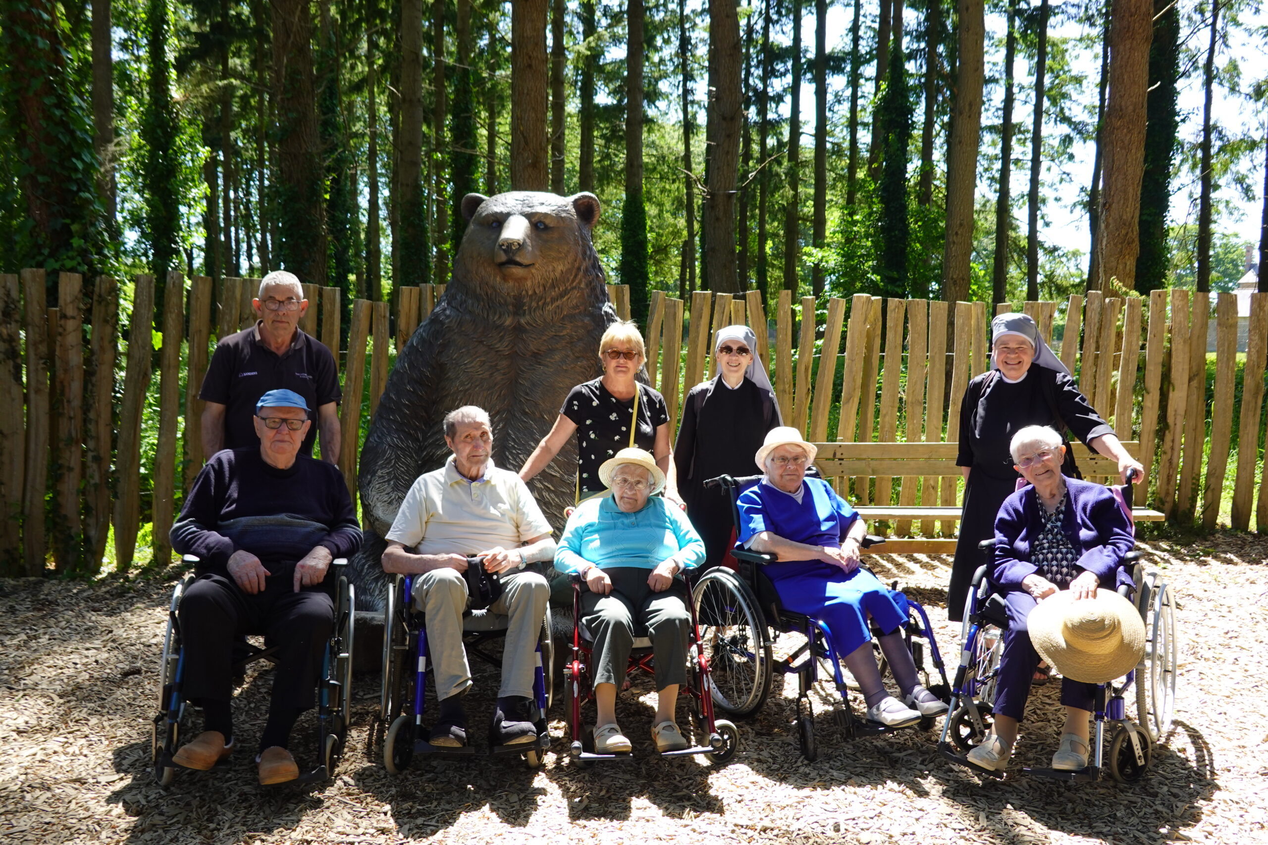 Personnes âgées au zoo devant une statue d'ours avec des petites sœurs des pauvres au soleil
